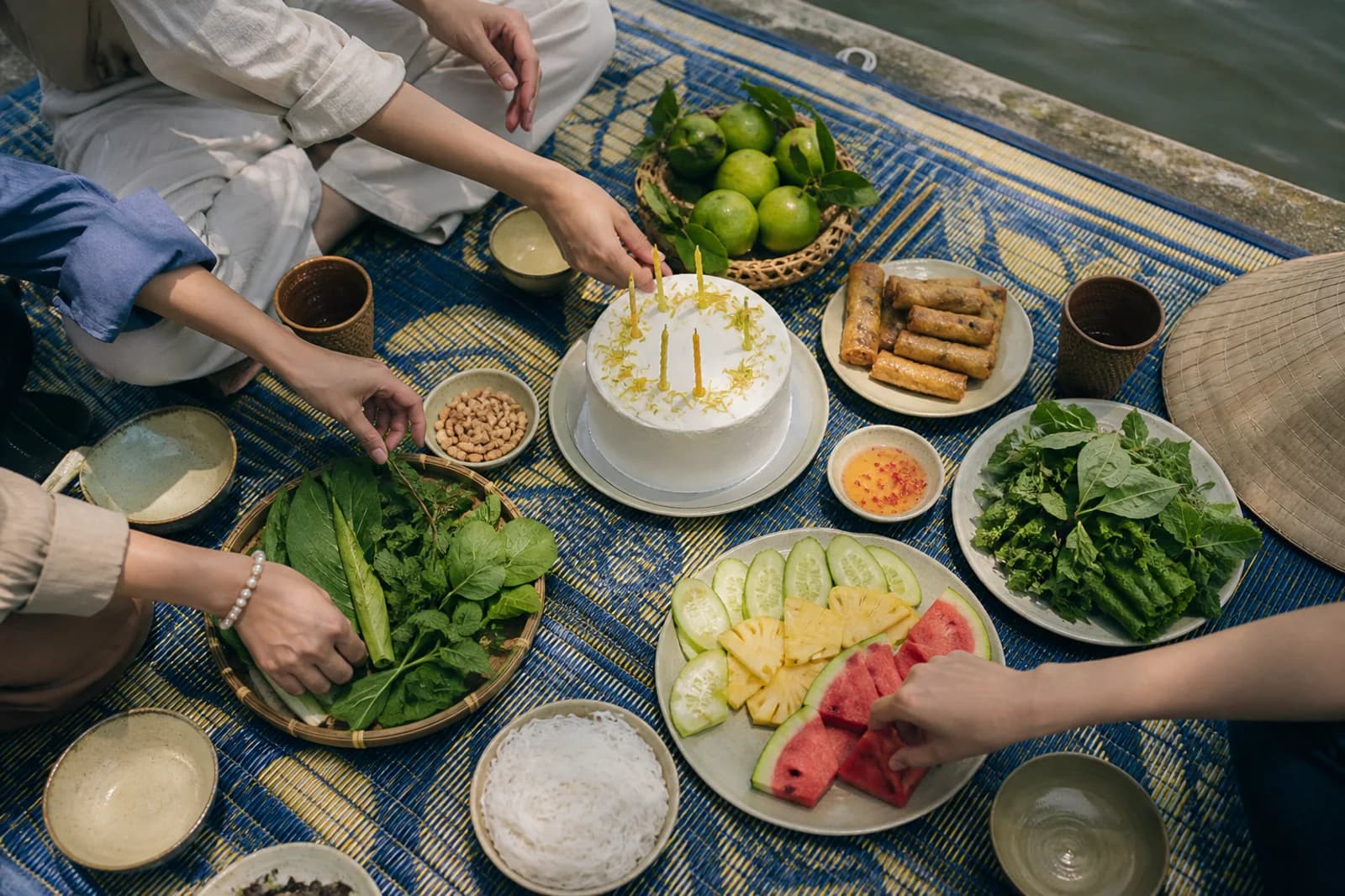 Bánh kem, món Việt và trái cây trên tấm bạt picnic